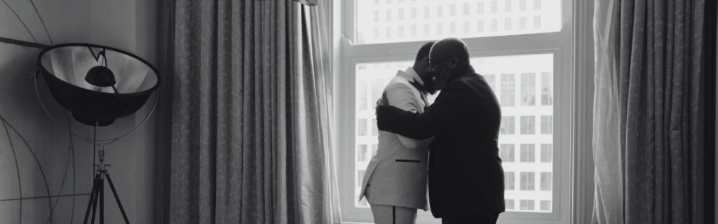 Deux hommes en costume l'un blanc et l'autre noir se faisant une accolade dans un appartement