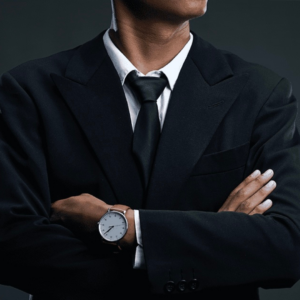 Buste homme en costume noir chemise blanche cravate noir et montre avec bracelet en cuir marron