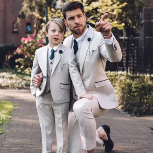 Un père et son petit garçon portant le meme smoking gris, le père pointant du doigt au loin pour guider le regard de son fils
